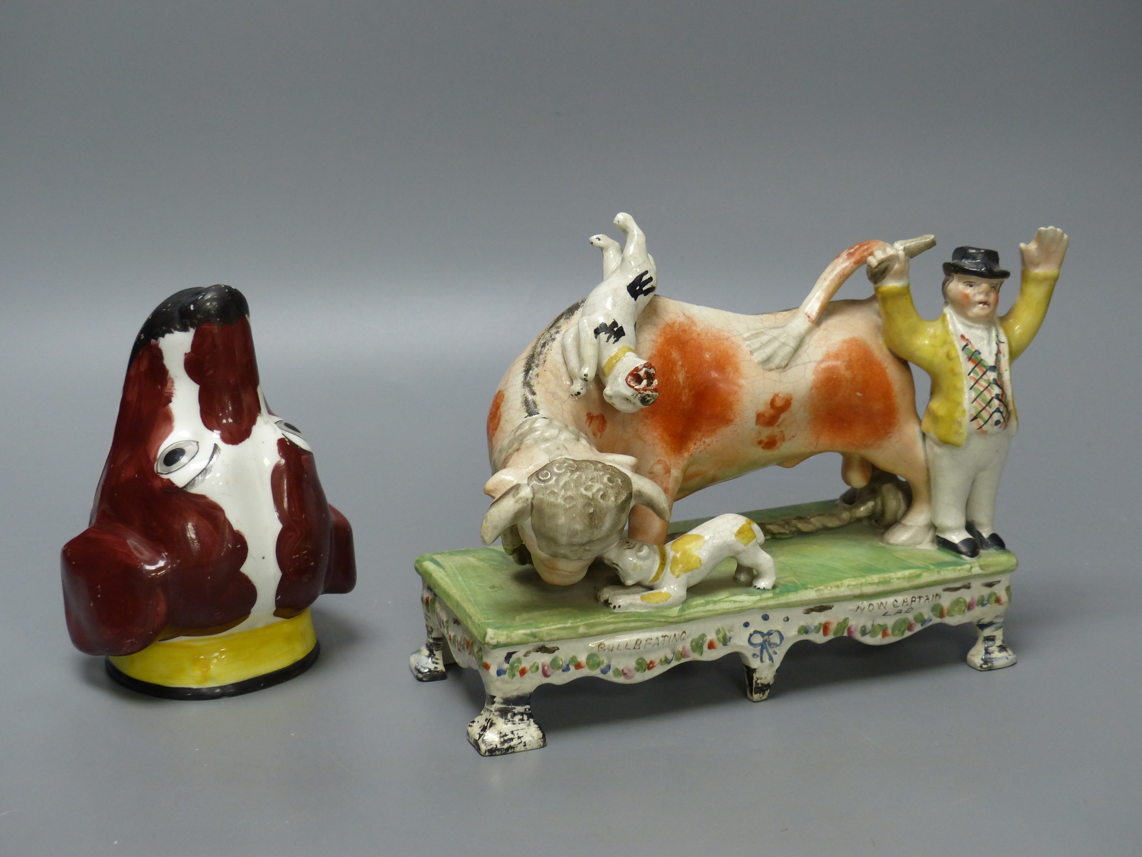 A 19th century Staffordshire bull baiting group, width 19cm, and a 19th century English porcelain spaniel’s head stirrup cup (2)